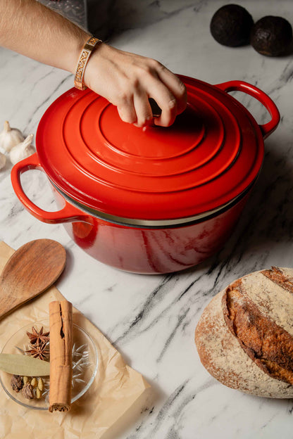 Red cast iron cookware on a marble surface with bread and spices.